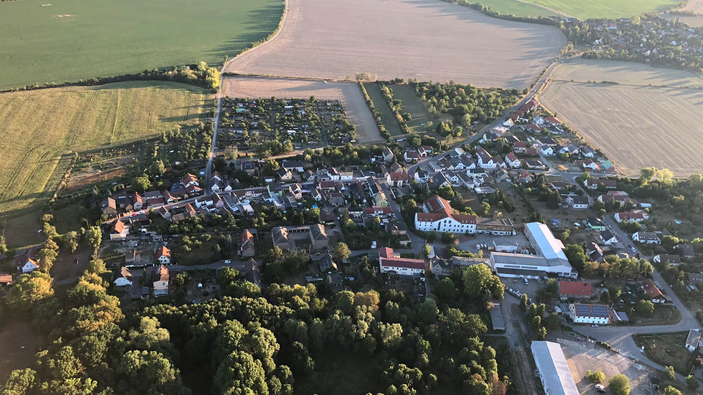 Luftbild von Zschölkau im Abendlicht, aufgenommen aus einem Heißluftballon: Häuser und Gärten des Dorfes, umgeben von Feldern und Wald